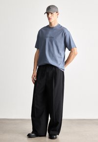 Svijetlo plava pamučna majica s logom "Calvin Klein", uparen s crnim širokim hlačama i crnim cipelama, dopunjen sivom kapom.