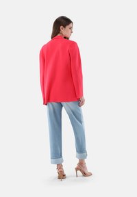 Helles rotes Blazer mit strukturiertem Design, kombiniert mit hellblauen Jeans mit hochgekrempelten Ärmeln und nude-farbenen Riemchen-Heels. Glatte Stofftextur.