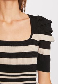 Haut rayé noir et beige avec un décolleté carré. Présente une texture côtelée, des manches courtes avec des accents volantés, et une coupe ajustée.