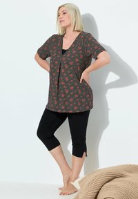 Top de corte holgado a rayas con un patrón floral rojo, escote en V y mangas cortas, combinado con leggings capri negros y pies descalzos.