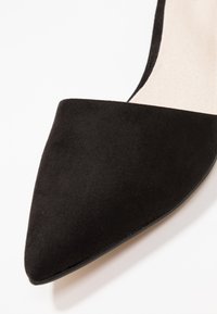 Black suede pointed-toe pump with a smooth texture, featuring a sleek, minimal design and a subtle inner lining in a light color.