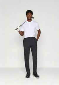 Golfklädsel med en figursydd vit pikétröja med tre knappar, kombinerad med skräddarsydda svarta byxor och svarta golfskor.