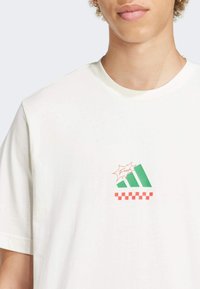 Witte katoenen t-shirt met een kleine groen en rode graphic met geruite accenten. Klassieke ronde hals en korte mouwen.