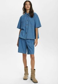 Blårandig denimskjorta med korta ärmar och två bröstfickor, kombinerad med matchande denimshorts. Bärs med bruna ankelstövlar.