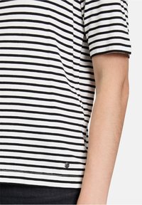 Sort-hvid stribet kortærmet skjorte lavet af bomuld, med en rund kant og et lille logo-akkent nær bunden.