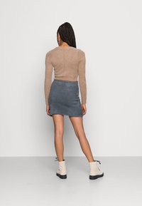 Camisola de mangas compridas felpuda em castanho claro, combinada com uma saia mini tricotada em cinza escuro e botas de tornozelo em bege com solas e atacadores pretos.