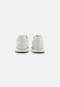 Hvite sneakers med en glatt læroverdel, rund hæl og gummisåle. Kjennetegn inkluderer minimal søm og polstret krage.