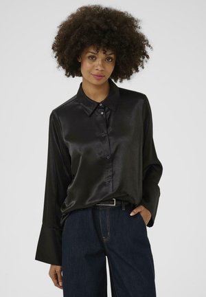 Chemise noire en satin à boutons, avec un col et des manches larges, assortie à un pantalon en denim foncé. Texture lisse avec un éclat subtil.