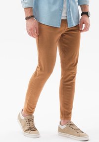 Pantalones de algodón marrón con un ajuste slim, combinados con zapatillas beige con acentos en crema y una superficie texturizada. Camisa de botones de color azul claro.