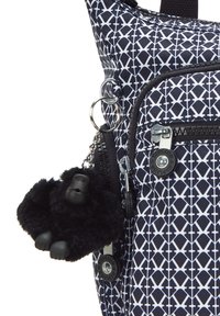 Bolso de patrones en blanco y negro con un bolsillo con cremallera en el frente y un llavero de gorila de peluche negro adjunto al tirador de la cremallera.