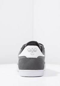 Sneaker grigio in suede con dettagli bianchi, collo imbottito e un logo sul tallone. Ha una suola in gomma e una forma elegante e arrotondata.