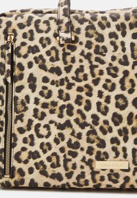 Kabelka se zvířecím vzorem leoparda vyrobená z umělé kožešiny, s kapsou na zip a zlatou brandovou destičkou. Texturovaný povrch s černými akcenty.