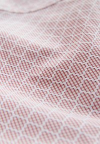 Textil mit einem roten geometrischen Muster auf weißem Hintergrund, mit einer glatten Textur und einem leichten, zerknitterten Aussehen.