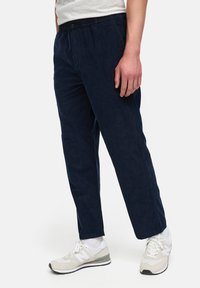 Marineblå kordfløyelsbukser med avslappet passform, elastisk midje og knappelukking. Stylet med hvite sneakers for et avslappet utseende.