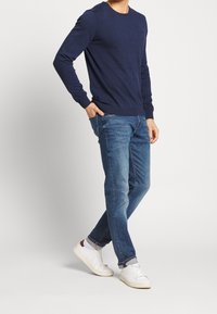 Marinblå tröja med lång ärm, rundad halsringning och åtsittande fåll. Kombineras med blå denimjeans och vita sneakers. Avslappnad outfit.