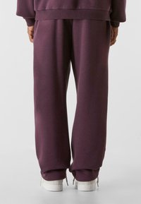 Lila Jogginghose aus weichem Stoff, mit einer lockeren Passform, elastischem Bund und deziliertem Kordelzug am Saum. Darunter weiße Sneaker.
