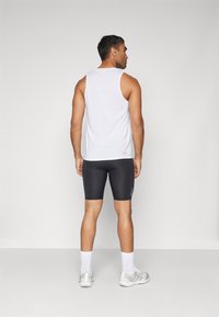 Valge sportlik tank top ja mustad kompressioonilühikesed püksid, millele on lisatud valged sokid ja hallid tossud; siledad tekstuurid ja lihtne disain.