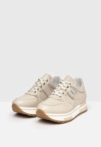 Sneakers in pelle beige con suole in gomma bianche e marroni, dotate di hardware metallico, lacci rotondi e colletto imbottito per il massimo comfort.