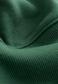 Zielona tkanina o miękkiej fakturze z prążkowanym wzorem. Materiał wydaje się być elastycznym dzianiną, ukazującym gładkie krzywe.