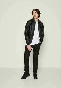 Μαύρο faux δερμάτινο jacket με φερμουάρ, φορεμένο πάνω από ένα λευκό πουκάμισο. Λεπτό μαύρο παντελόνι και μαύρα αθλητικά ολοκληρώνουν την εμφάνιση.