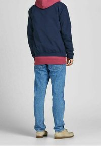 Námořnická bomber bunda přes vínovou mikinu s kapucí, kombinovaná se světle modrými džínami a béžovými botami. Bunda má elastické manžety a lem.