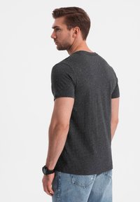 Mørkegrå t-shirt med korte ærmer, spottet mønster, afslappet pasform og rund halsudskæring. Bæres med lyseblå denimjeans.
