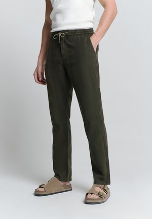 Olijfgroene broek met elastische tailleband en trekkoord, met zijzakken en een rechtgesneden poot. G gedragen met beige instapsandalen.