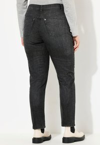 Jeans in denim grigio scuro con gamba affusolata, dotati di tasche posteriori e vita a media altezza, abbinati a stivali alla caviglia beige.