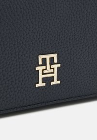 Borsa in pelle testurizzata blu navy con logo in tonalità oro. Il primo piano evidenzia la superficie morbida e il particolare dettaglio del marchio.