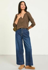 Brown, long-sleeve top with a V-neck and button accents, paired with wide-leg blue denim pants and tan slip-on shoes.