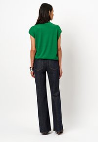 Groen top met korte mouwen gecombineerd met donkerblauwe wijde jeans. De jeans hebben een klassiek ontwerp voor de achterzak. Glad oppervlak overal.