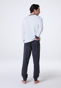 Camicia a maniche lunghe blu chiaro con polsini blu scuro, abbinata a pantaloni jogger grigi scuri con tasche laterali e una vestibilità comoda.