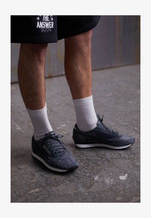 Tumed hallid spordijalatsid tekstuuriga kangast, paelad ja valge kummitald. Koos valgete põlvikutega betoonpinnal.