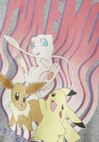 Camiseta gris con personajes de Pokémon: Mew con ojos azules, Eevee con pelaje marrón claro y Pikachu en amarillo con acentos negros.