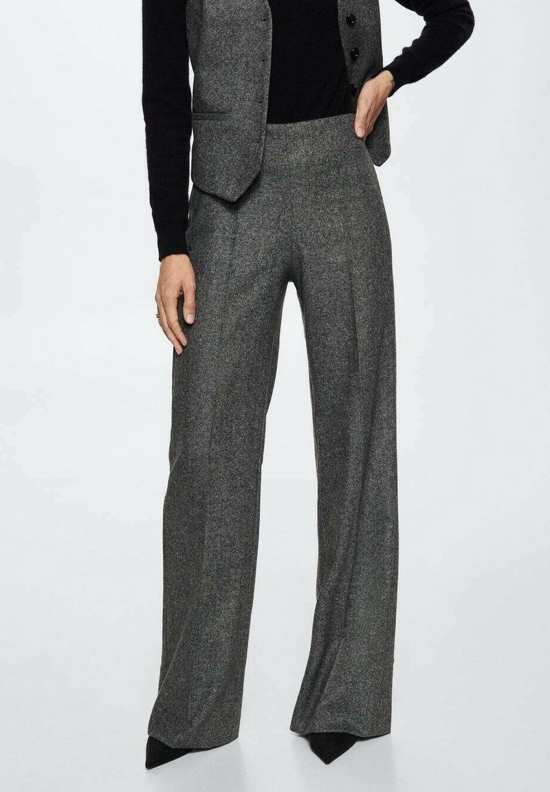 Pantalon à jambes larges en tissu gris texturé, avec une taille haute et des plis subtils, associé à un haut noir ajusté et un gilet.