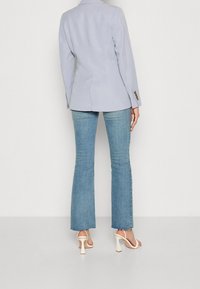 Jasnoszara, dopasowana marynarka o usztywnionej formie, zestawiona z jasnoniebieskimi spodniami dzwoniącymi; modelka nosi jasne szpilki. Marynarka ma mankiety zapinane na guziki.