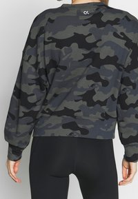 Sweatshirt gris camouflage avec manches longues, coupe décontractée et bords ribdés. Présente un petit logo à l'arrière près de l'encolure.