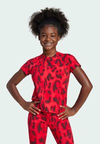Camiseta deportiva roja con estampado animal negro, de mangas cortas y cuello redondo, combinada con leggings a juego que presentan el mismo patrón.