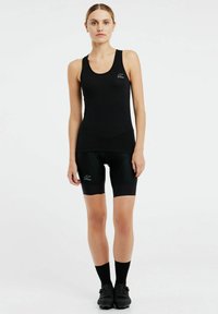 Top sportivo nero abbinato a pantaloni bici neri, entrambi con un design aderente e dettagli di logo sottili. Gli accessori includono calze e scarpe nere.