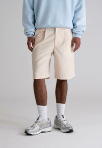 Light beige shorts with pleats, paired with a pale blue sweatshirt and silver athletic shoes. White socks complete the look.