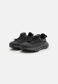 Scarpe da ginnastica nere con parte superiore in rete, lacci bungee regolabili e suola sagomata con dettagli ritagliati per ventilazione e grip.
