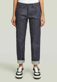 Vaqueros de mezclilla oscura con pierna recta, dobladillos enrollados y costuras contrastantes. Combinados con zapatillas clásicas en blanco y negro.