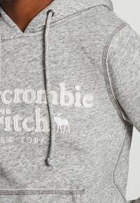 Grijze hoodie van zacht, textuurstof met een voorzak, voorzien van witte geborduurde letters en een klein hertenlogo.