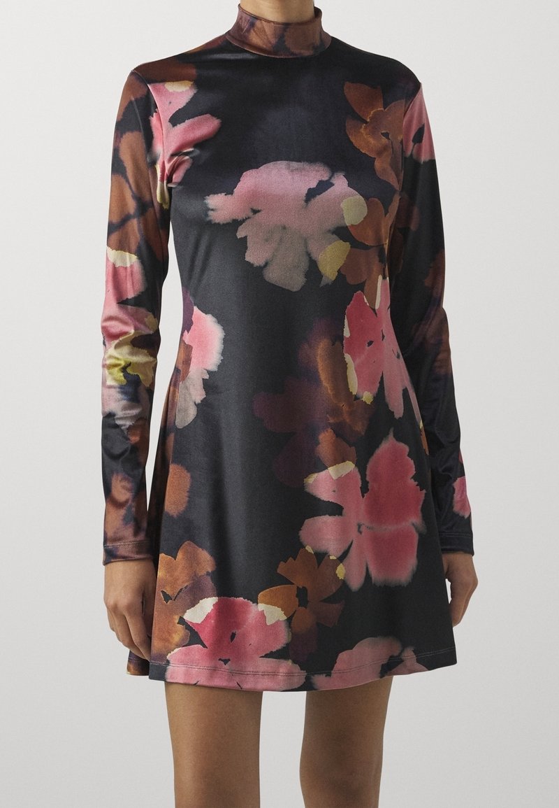 Robe à manches longues et col montant avec une base noire et de grands motifs floraux roses, marron et orange, portée à mi-cuisse.