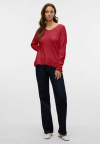 Pull rouge à col en V avec une coupe décontractée, manches longues, texture côtelée et un ourlet légèrement court ; associé à un jean droit bleu foncé.