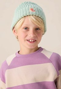 Un bonnet tricoté bleu clair avec une texture côtelée et une petite patch ; associé à un sweat-shirt rayé violet et crème.