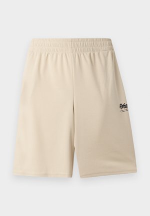 Deux mannequins portant des shorts longs beige assortis, des chaussettes blanches, des baskets blanches et des T-shirts blancs avec un petit texte noir, debout devant un fond blanc.