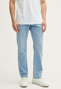 Lichtblauwe denim jeans met een rechte pasvorm, een vervaagde wassing en contrasterende stiksels. Gecombineerd met witte sneakers en een simpel wit T-shirt.