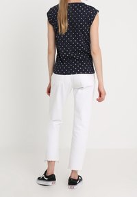 Námořnický top s krátkým rukávem a bílým vzorem, spárovaný s bílými zkrácenými džíny. Černé tenisky s bílými akcenty. Minimalistický design, volný střih.