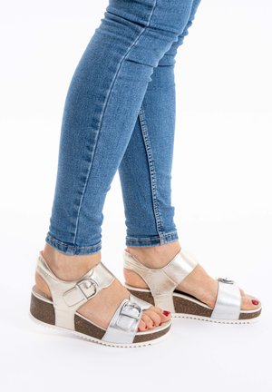 Platform sandals with silver metallic upper, adjustable buckles, and cork-like base. Features open toe and heel design.